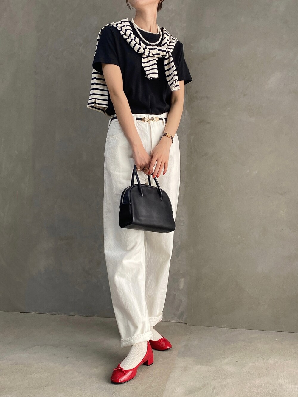 ブラック系のボストンバッグ、レッド系のパンプス、ホワイト系のデニムパンツを着用したレディースの夏コーディネートの2枚目の写真