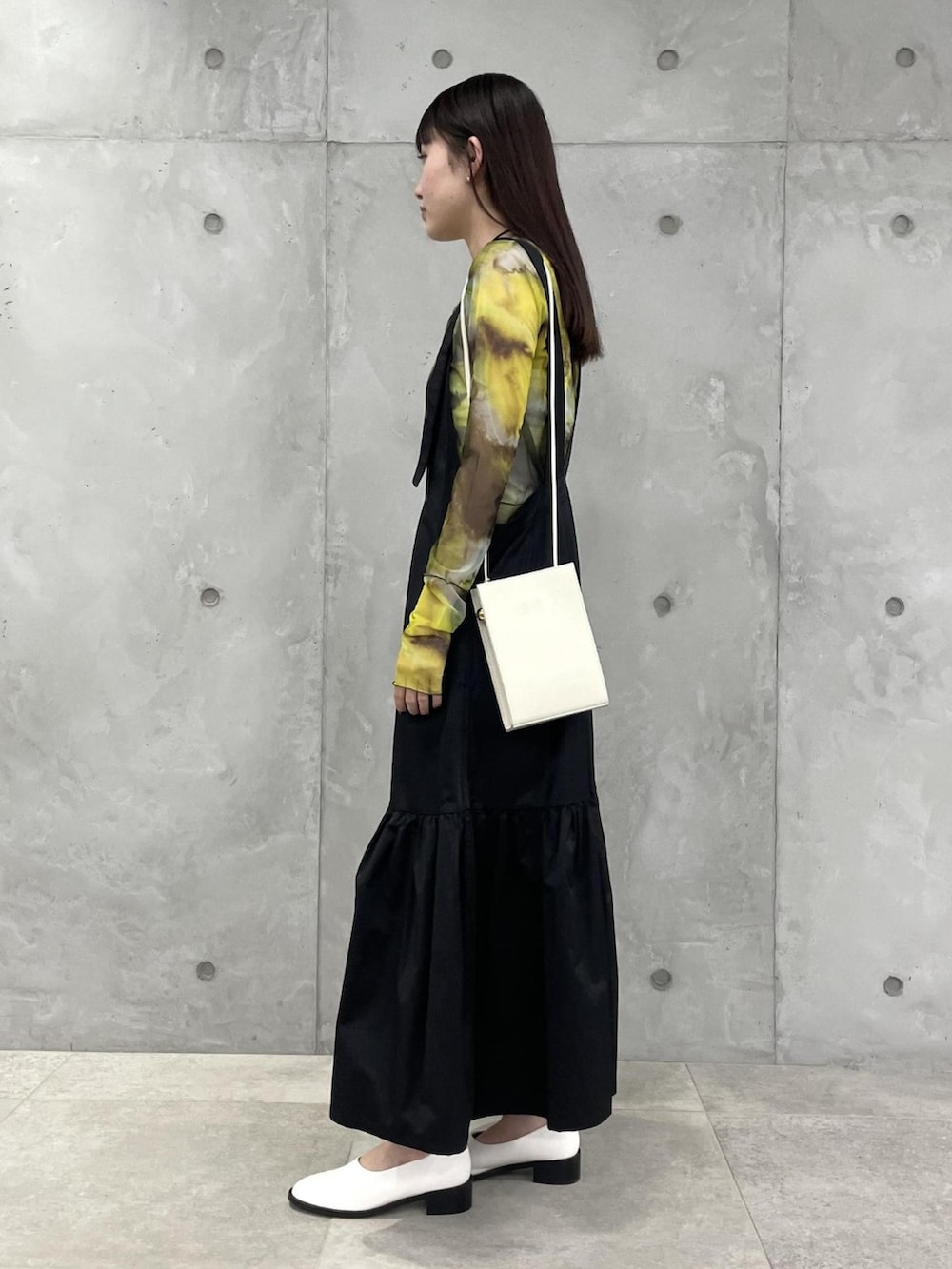 ブラック系のジャンパースカート、イエロー系のカーディガン/ボレロ、グレー系のショルダーバッグを着用したレディースの春コーディネートの2枚目の写真