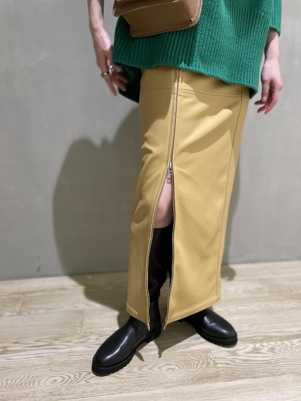 グリーン系のニット/セーター、ベージュ系のスカート、ブラック系のブーツを着用したレディースの夏コーディネートの5枚目の写真