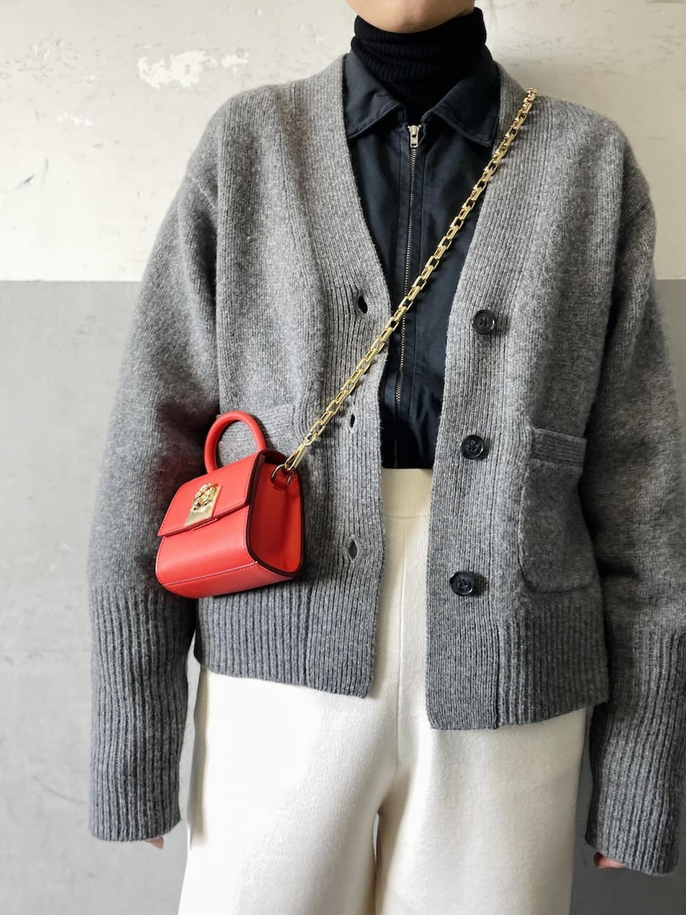 オレンジ系のショルダーバッグ、グレー系のカーディガン/ボレロ、ホワイト系のその他パンツを着用したレディースの冬コーディネートの4枚目の写真