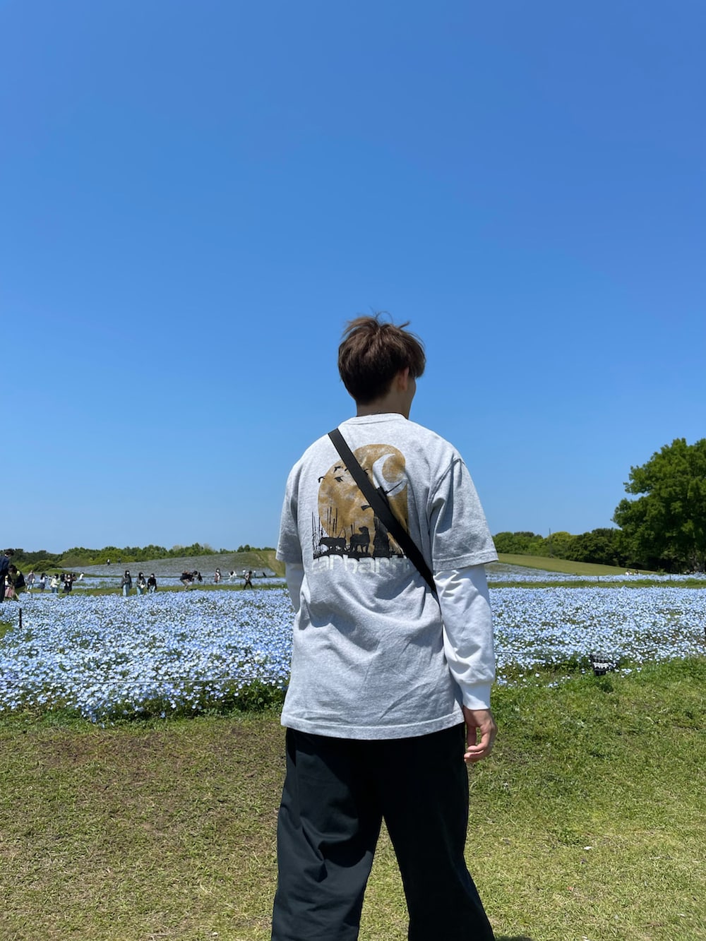 グレー系のTシャツ/カットソー、ホワイト系のスニーカー、ブラック系のショルダーバッグを着用したメンズの春コーディネートの2枚目の写真
