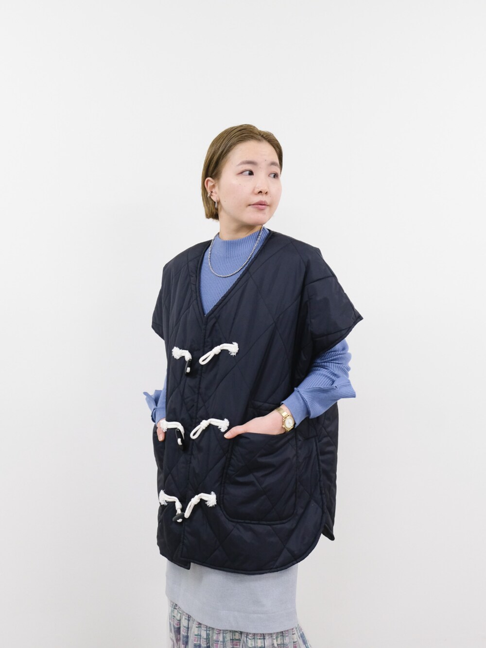 ブラック系のベスト、ブルー系のニット/セーター、ホワイト系のスカートを着用したレディースの冬コーディネートの2枚目の写真