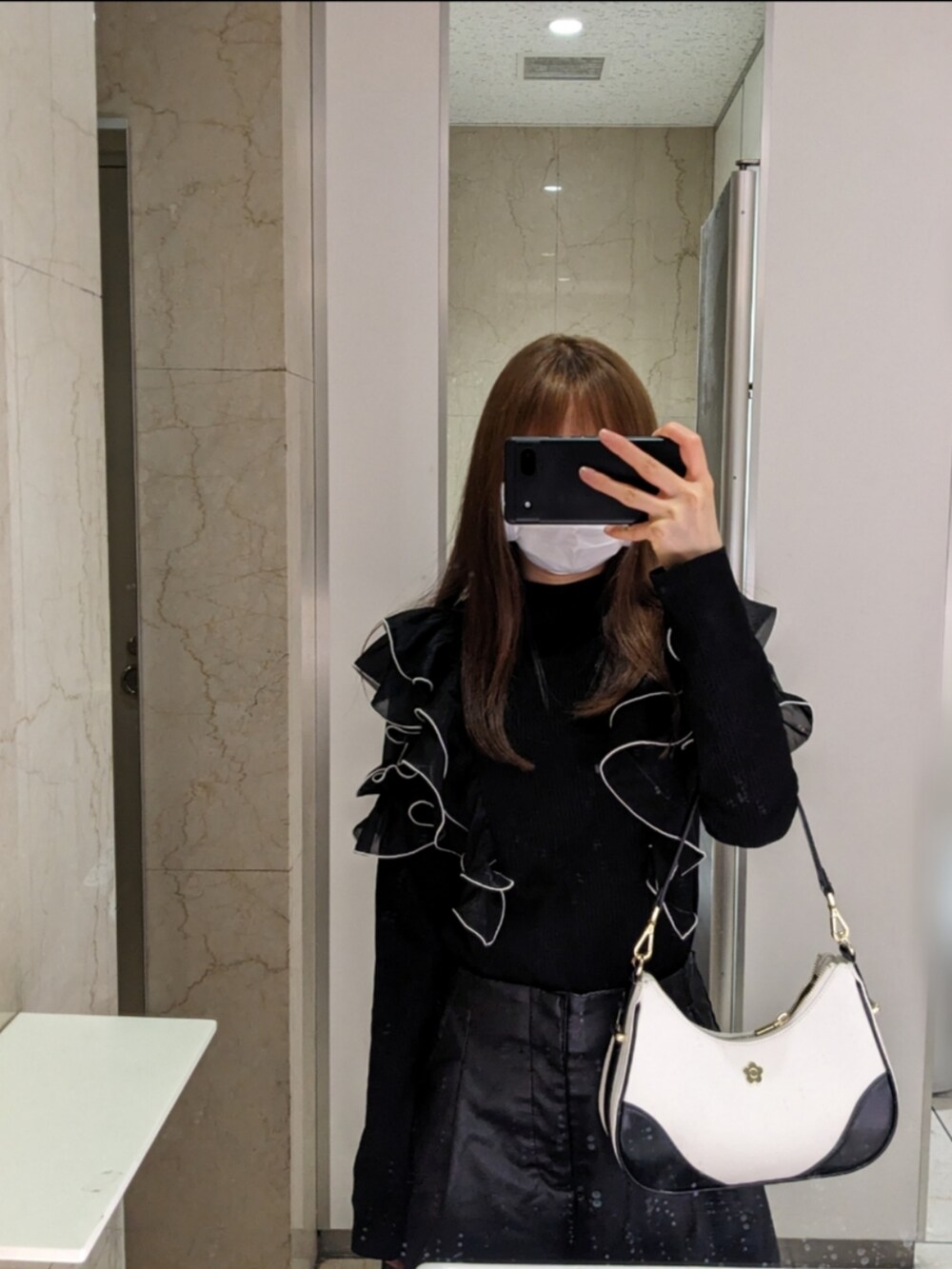 ブラック系のトップス、ブラック系のパンツ、ホワイト系のハンドバッグを着用したレディースの春コーディネートの2枚目の写真