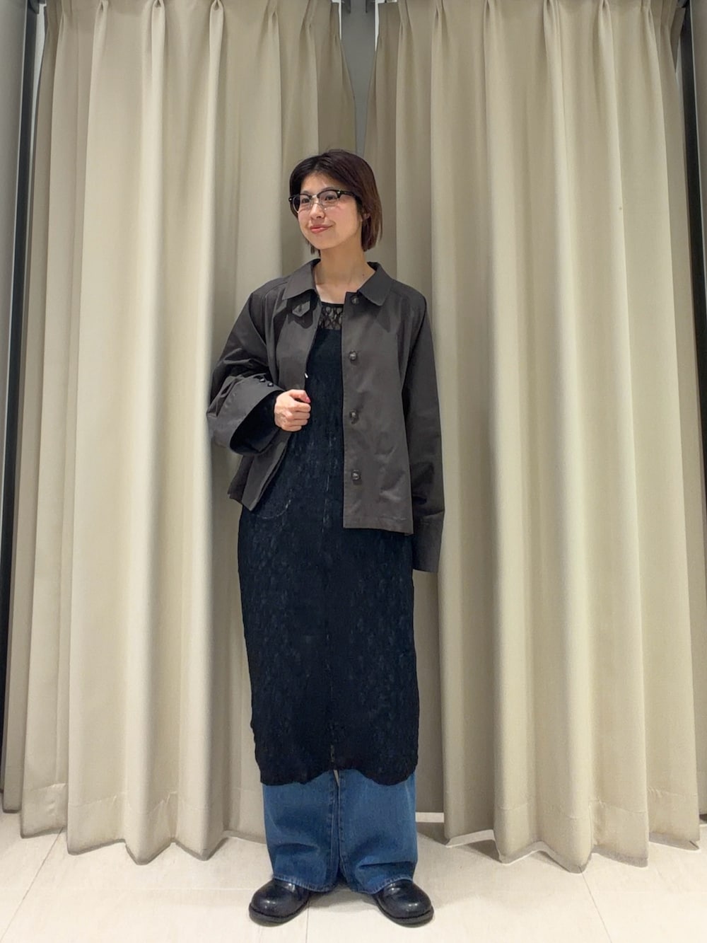 グレー系のステンカラーコート、ブラック系のワンピース、ブルー系のデニムパンツを着用したレディースの春コーディネートの2枚目の写真