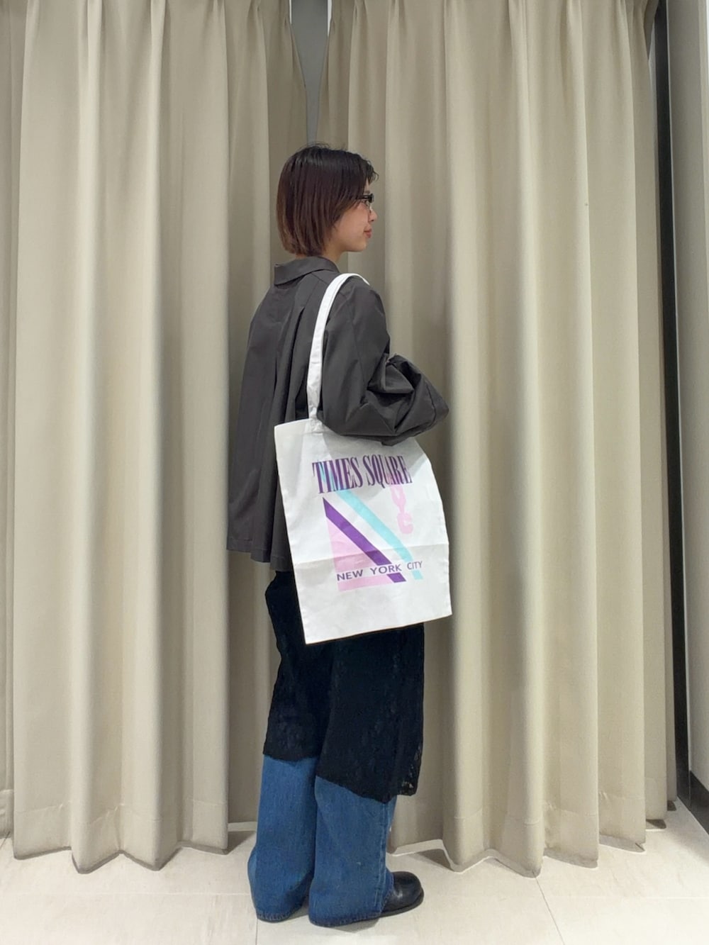 グレー系のステンカラーコート、ブラック系のワンピース、ブルー系のデニムパンツを着用したレディースの春コーディネートの4枚目の写真