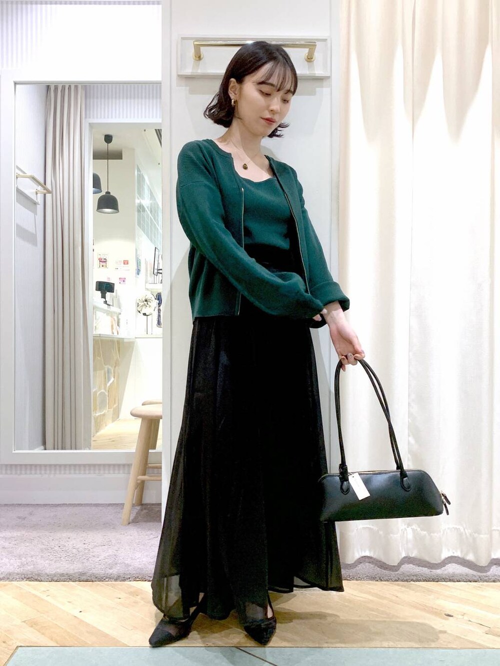 グレー系のスカート、ブラック系のボストンバッグ、グリーン系のカーディガン/ボレロを着用したレディースの夏コーディネートの2枚目の写真