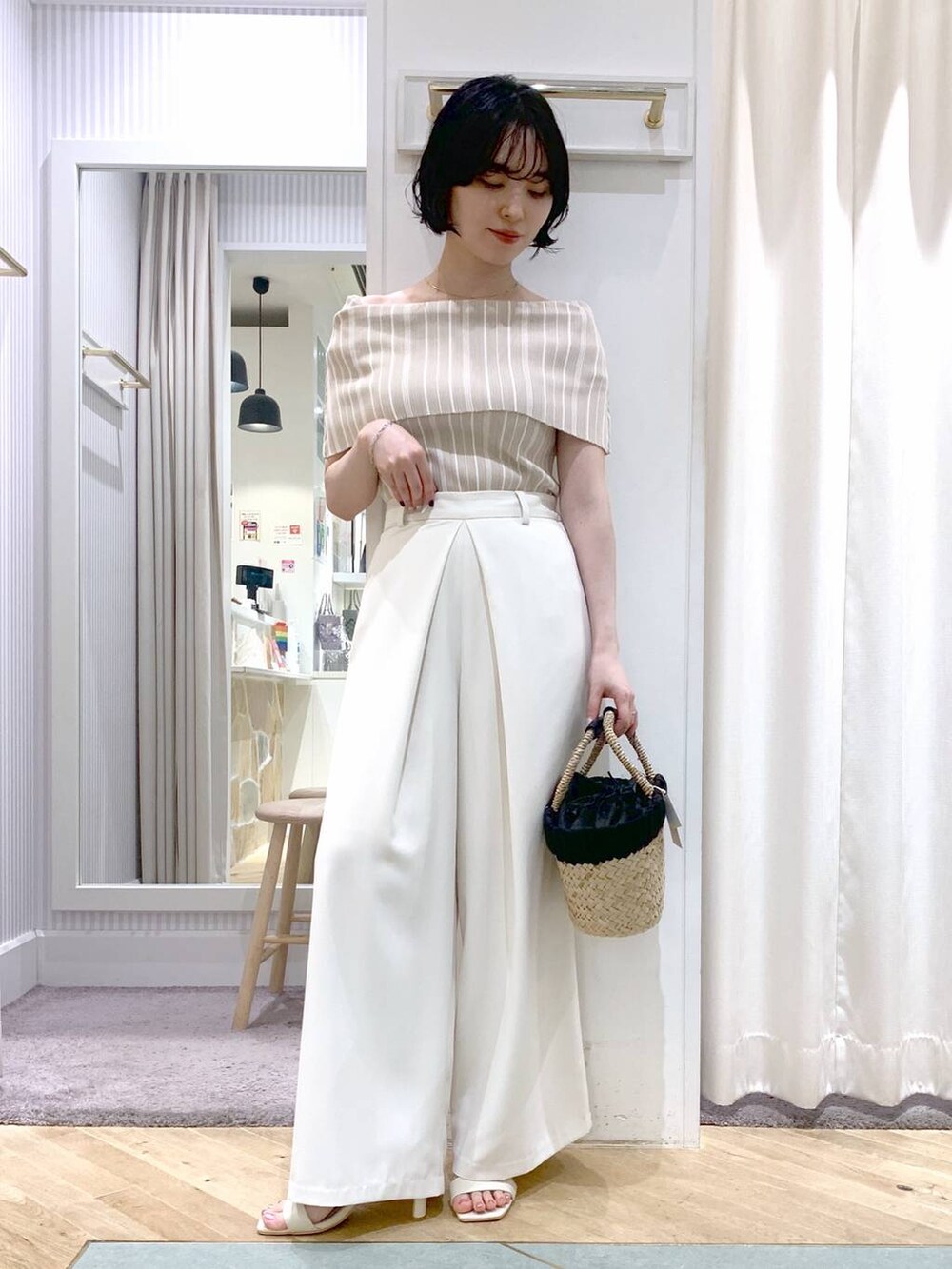 ベージュ系のかごバッグ、ホワイト系のサンダル、ホワイト系のスラックスを着用したレディースの夏コーディネートの2枚目の写真