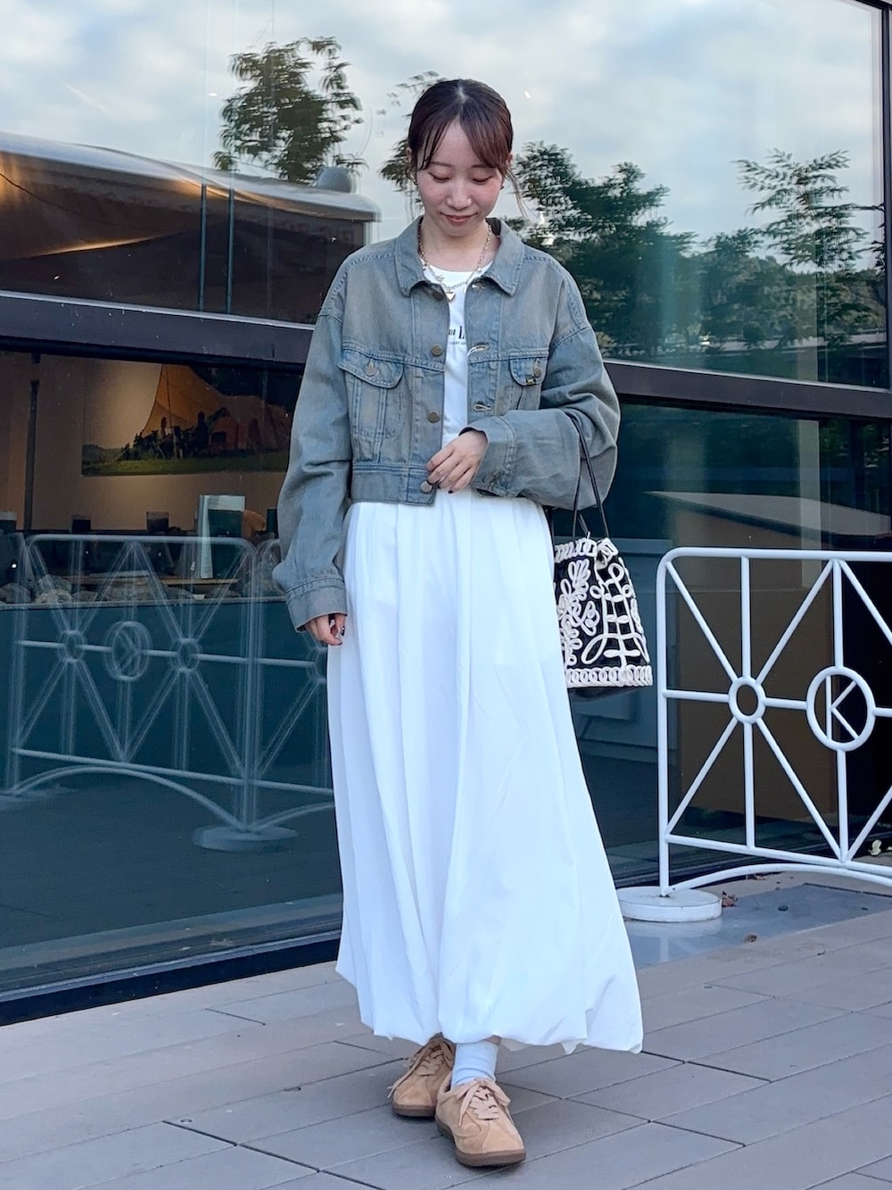 ブラウン系のデニムジャケット、ホワイト系のスカート、ベージュ系のスニーカーを着用したレディースの秋コーディネートの2枚目の写真