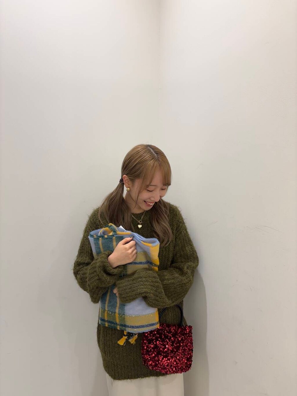 レッド系のショルダーバッグ、グリーン系のニット/セーター、ベージュ系のスカートを着用したレディースの冬コーディネートの2枚目の写真