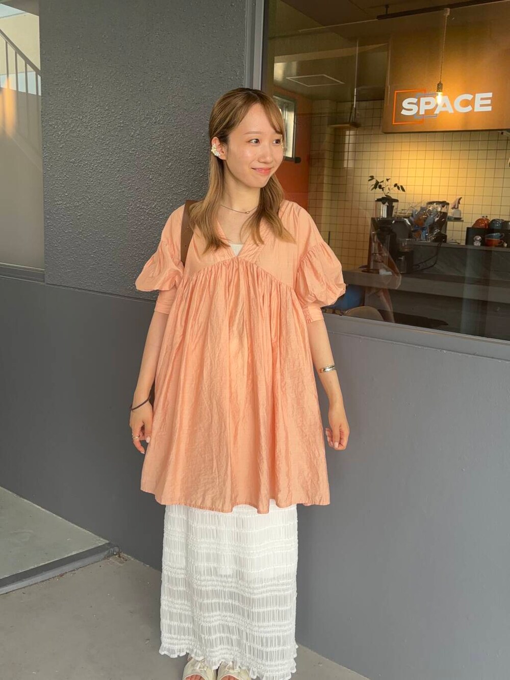 オレンジ系のワンピース、ホワイト系のスカート、ゴールド系のバングル/リストバンドを着用したレディースの夏コーディネートの2枚目の写真