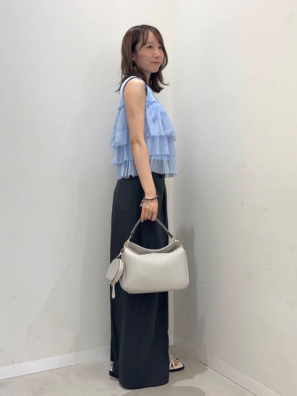 グレー系のショルダーバッグ、ブルー系のニット/セーター、ホワイト系のサンダルを着用したレディースの夏コーディネートの2枚目の写真