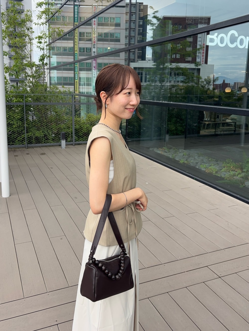 ベージュ系のベスト、ホワイト系のスカート、ブラウン系のショルダーバッグを着用したレディースの夏コーディネートの3枚目の写真