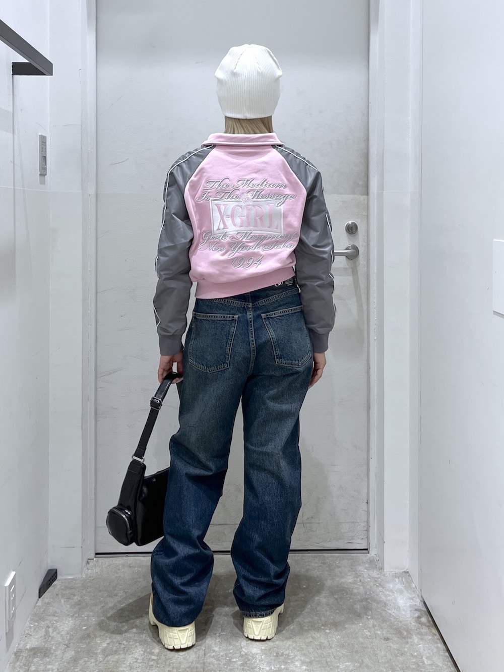 ピンク系のスウェット、ブルー系のデニムパンツ、ブラック系のショルダーバッグを着用したレディースの春コーディネートの2枚目の写真