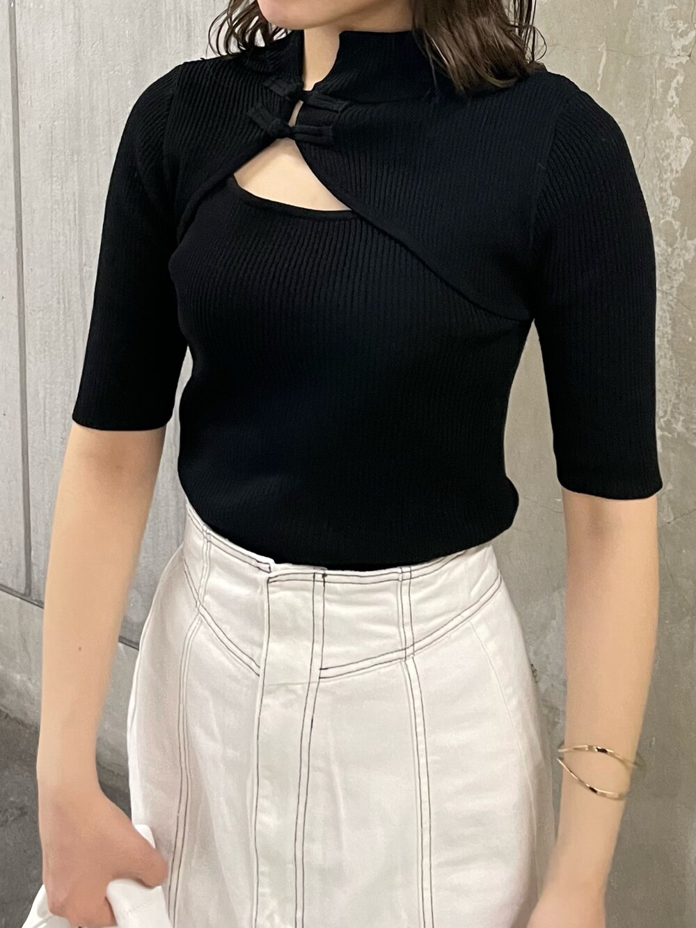 ブラック系のニット/セーター、ホワイト系のデニムスカート、ホワイト系のハンドバッグを着用したレディースの春コーディネートの4枚目の写真