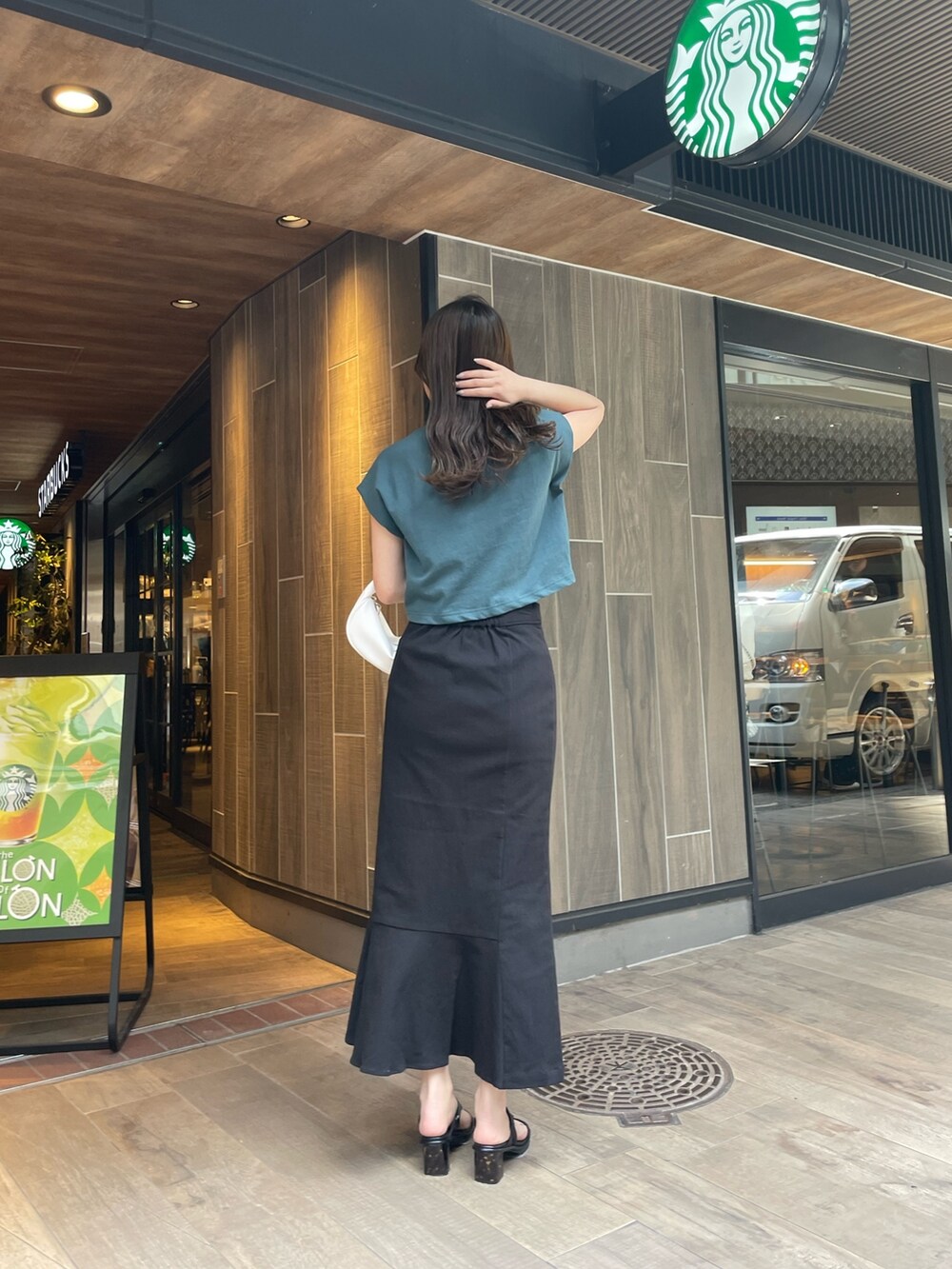 グリーン系のTシャツ/カットソー、ブラック系のスカート、ホワイト系のハンドバッグを着用したレディースの春コーディネートの3枚目の写真