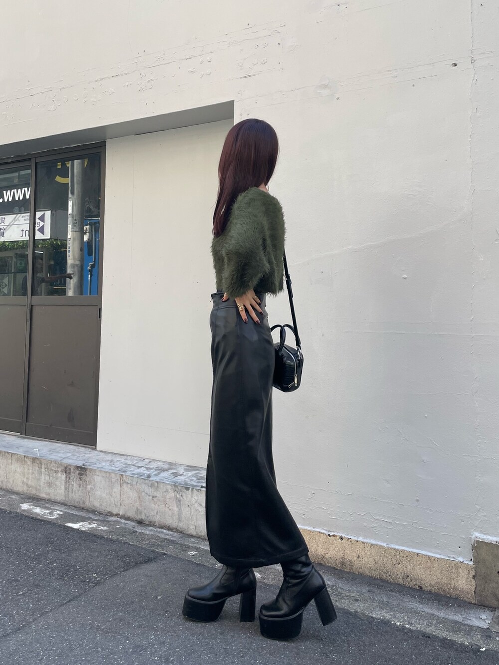 グリーン系のニット/セーター、ブラック系のボストンバッグ、ブラック系のスカートを着用したレディースの秋コーディネートの2枚目の写真