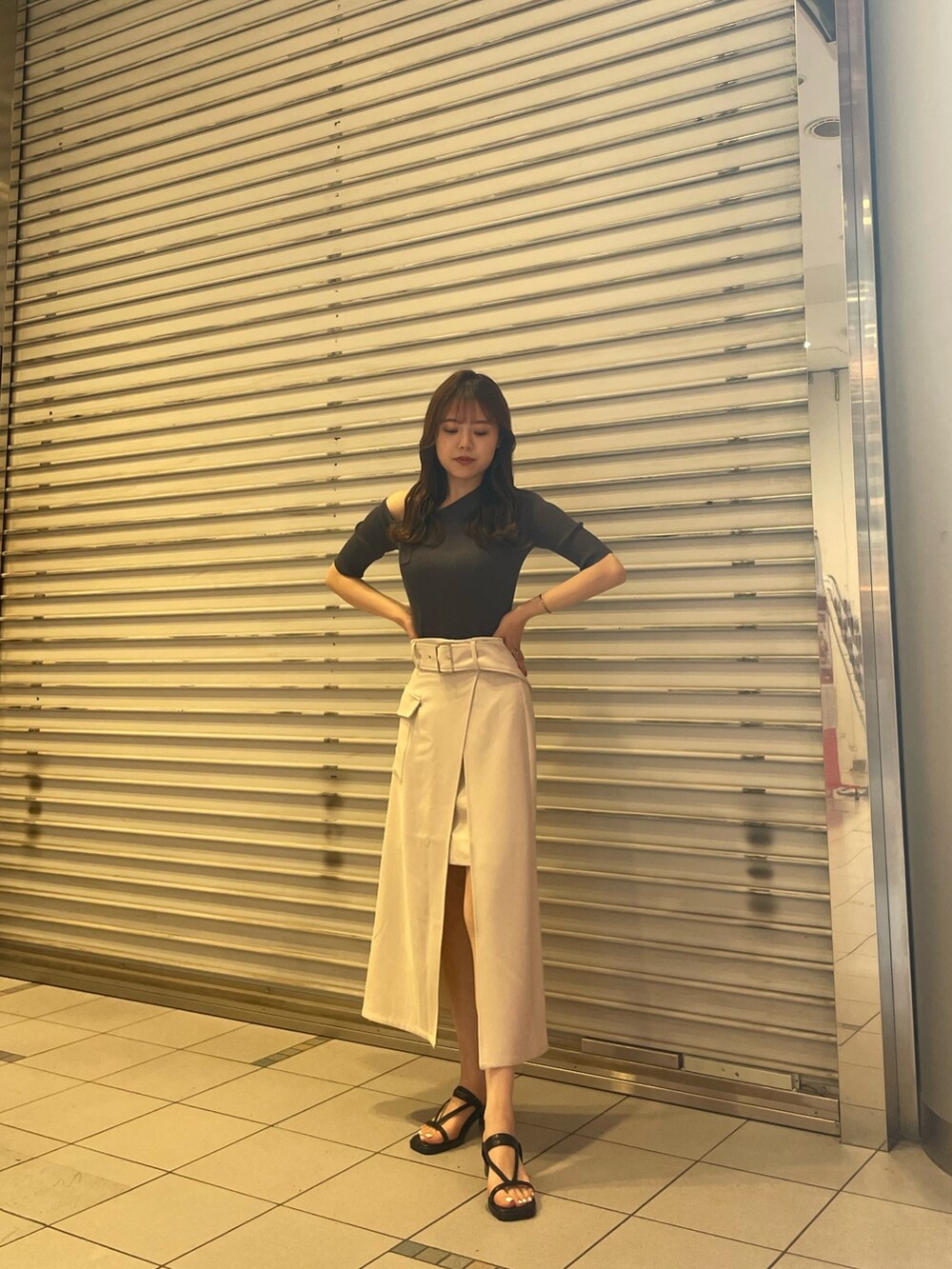 グレー系のニット/セーター、ホワイト系のスカート、ブラック系のサンダルを着用したレディースの春コーディネートの2枚目の写真