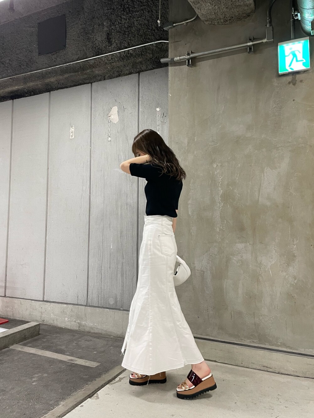 ブラック系のニット/セーター、ホワイト系のデニムスカート、ホワイト系のハンドバッグを着用したレディースの春コーディネートの2枚目の写真