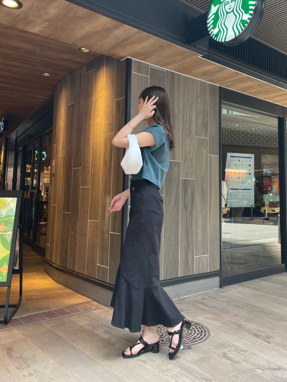 グリーン系のTシャツ/カットソー、ブラック系のスカート、ホワイト系のハンドバッグを着用したレディースの春コーディネートの2枚目の写真