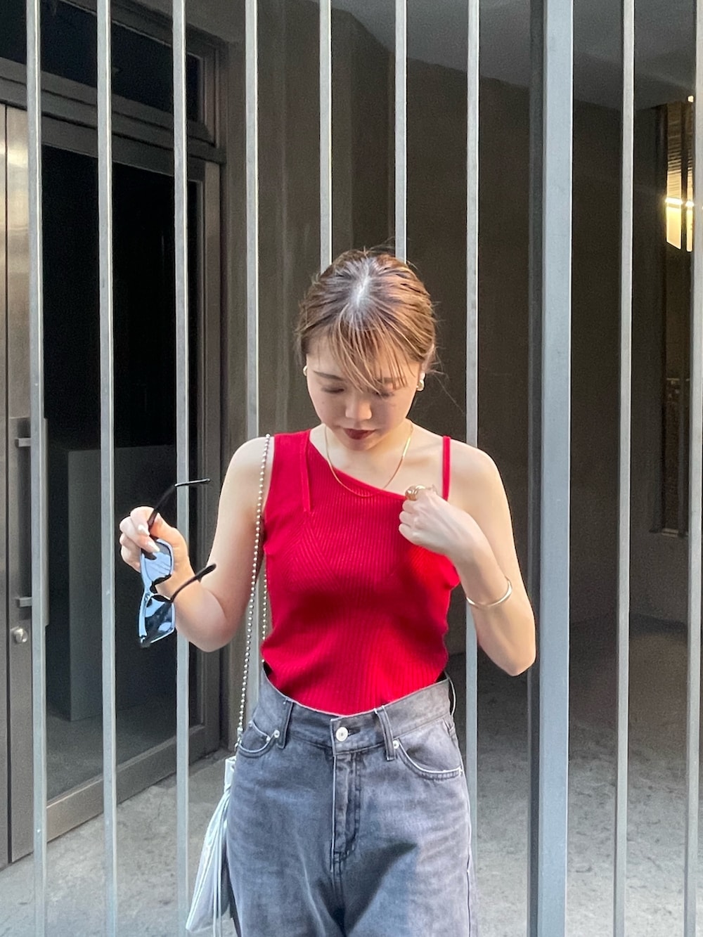 レッド系のニット/セーター、ブラック系のサンダル、ブラック系のデニムパンツを着用したレディースの春コーディネートの4枚目の写真