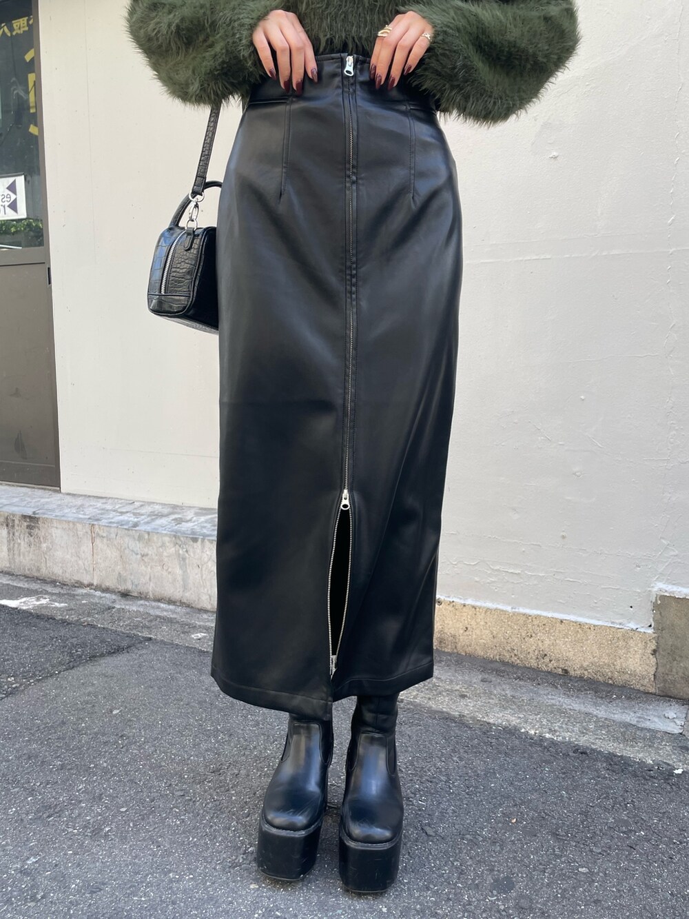 グリーン系のニット/セーター、ブラック系のボストンバッグ、ブラック系のスカートを着用したレディースの秋コーディネートの7枚目の写真