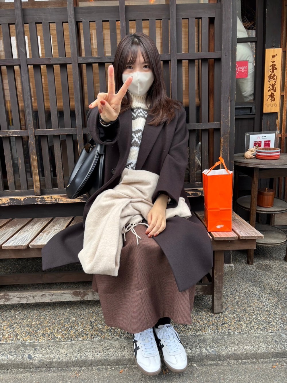 ホワイト系のベスト、ブラウン系のスカート、ホワイト系のスニーカーを着用したレディースの冬コーディネートの2枚目の写真