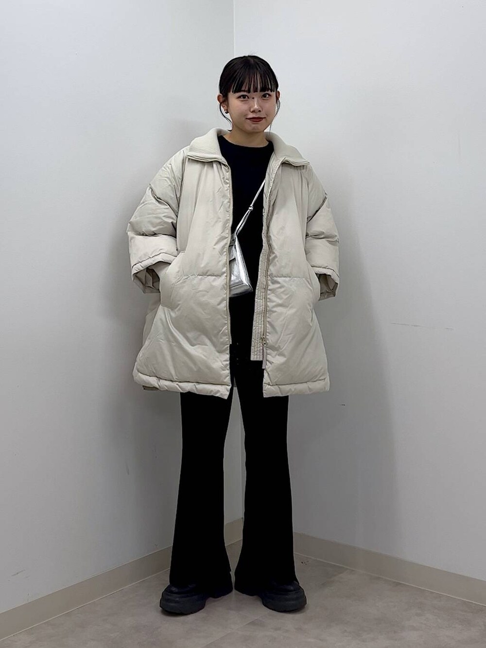 シルバー系のショルダーバッグ、ホワイト系のポンチョ、ブラック系のTシャツ/カットソーを着用したレディースの秋コーディネートの2枚目の写真