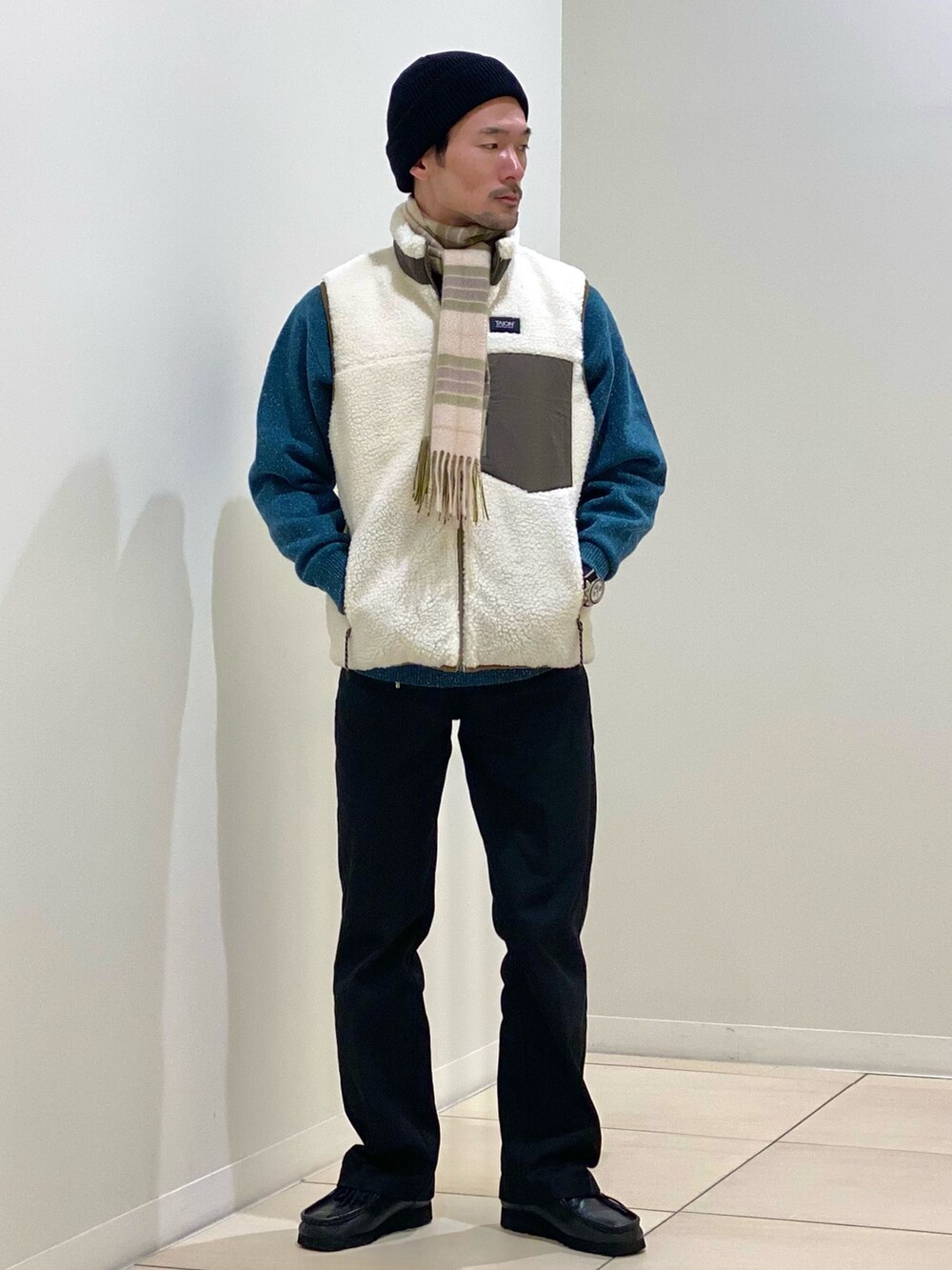 ホワイト系のダウンベスト、グリーン系のニット/セーター、グリーン系のマフラーを着用したメンズの冬コーディネートの2枚目の写真