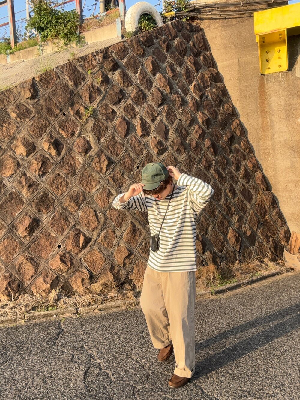 グリーン系のTシャツ/カットソー、ブラック系のショルダーバッグ、ベージュ系のチノパンツを着用したメンズの春コーディネートの2枚目の写真
