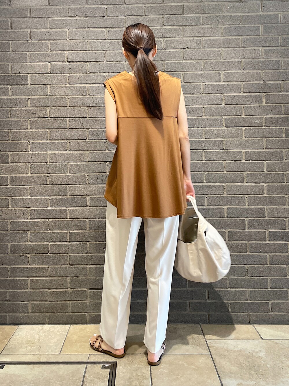 イエロー系のTシャツ/カットソー、ブラック系のトートバッグ、ホワイト系のスラックスを着用したレディースの夏コーディネートの3枚目の写真