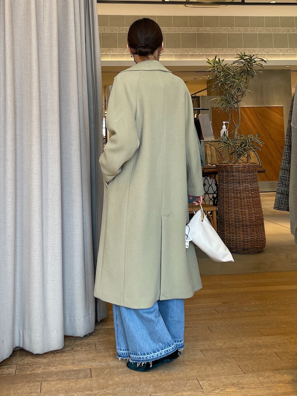 ホワイト系のトートバッグ、ブルー系のデニムパンツ、グリーン系のチェスターコートを着用したレディースの冬コーディネートの3枚目の写真