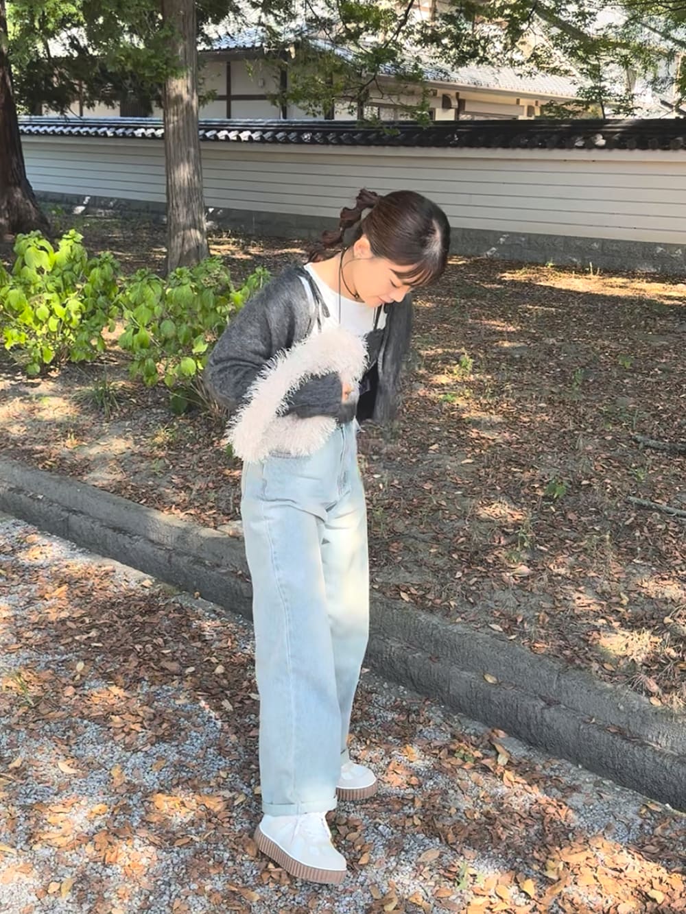 グレー系のカーディガン/ボレロ、ブルー系のデニムパンツ、ホワイト系のバッグを着用したレディースの秋コーディネートの2枚目の写真