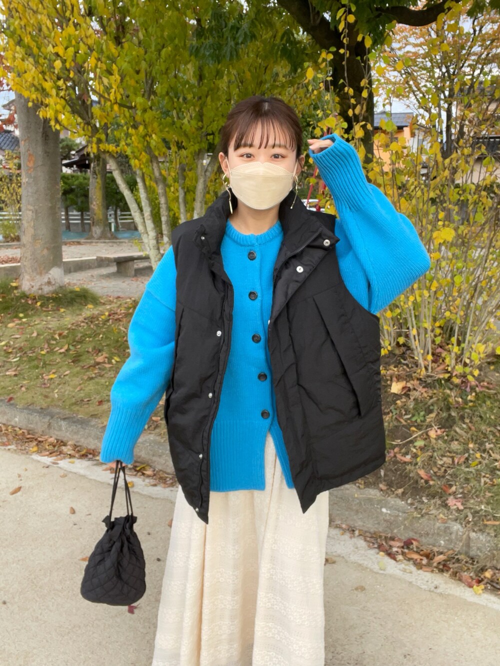 ベージュ系のスカート、ブルー系のカーディガン/ボレロ、ブラック系のダウンベストを着用したレディースの秋コーディネートの3枚目の写真