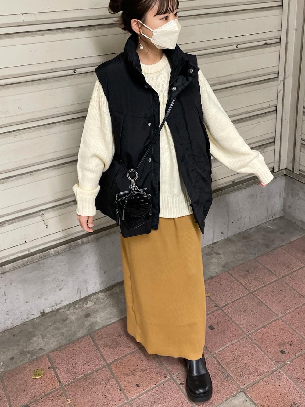 ホワイト系のニット/セーター、ブラック系のダウンベスト、イエロー系のスカートを着用したレディースの秋コーディネートの5枚目の写真