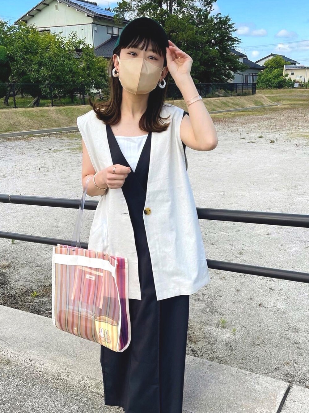 ブラック系のワンピース、ベージュ系のベスト、ホワイト系のトートバッグを着用したレディースの夏コーディネートの5枚目の写真