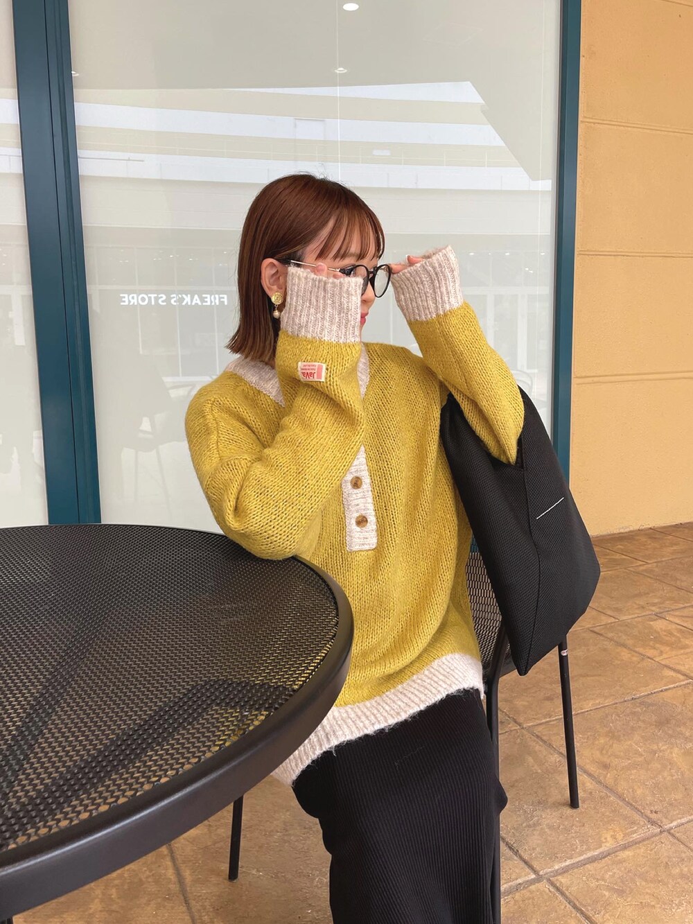 イエロー系のニット/セーター、ブラック系のトートバッグ、ブラック系のブーツを着用したレディースの秋コーディネートの2枚目の写真