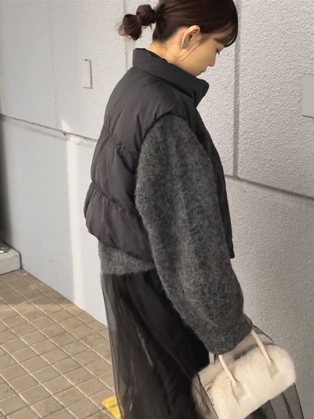 グレー系のワンピース、ブラック系のダウンベスト、ホワイト系のバッグを着用したレディースの冬コーディネートの2枚目の写真