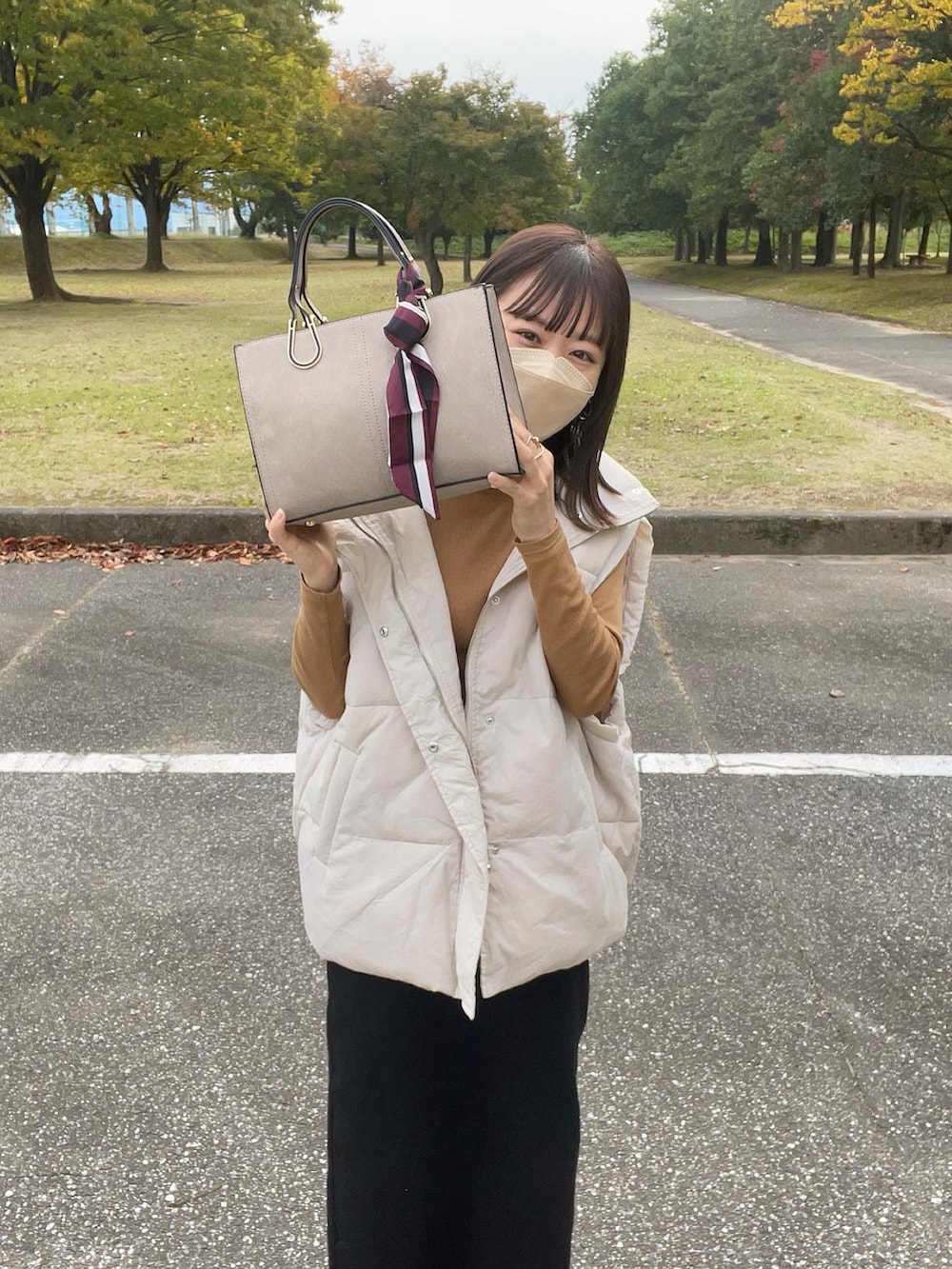 ベージュ系のバッグ、ホワイト系のダウンベスト、イエロー系のトップスを着用したレディースの秋コーディネートの2枚目の写真