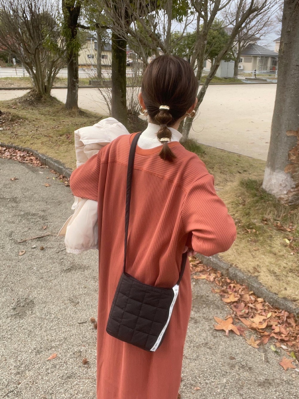 オレンジ系のワンピース、ホワイト系のニット/セーター、ブラック系のショルダーバッグを着用したレディースの冬コーディネートの4枚目の写真