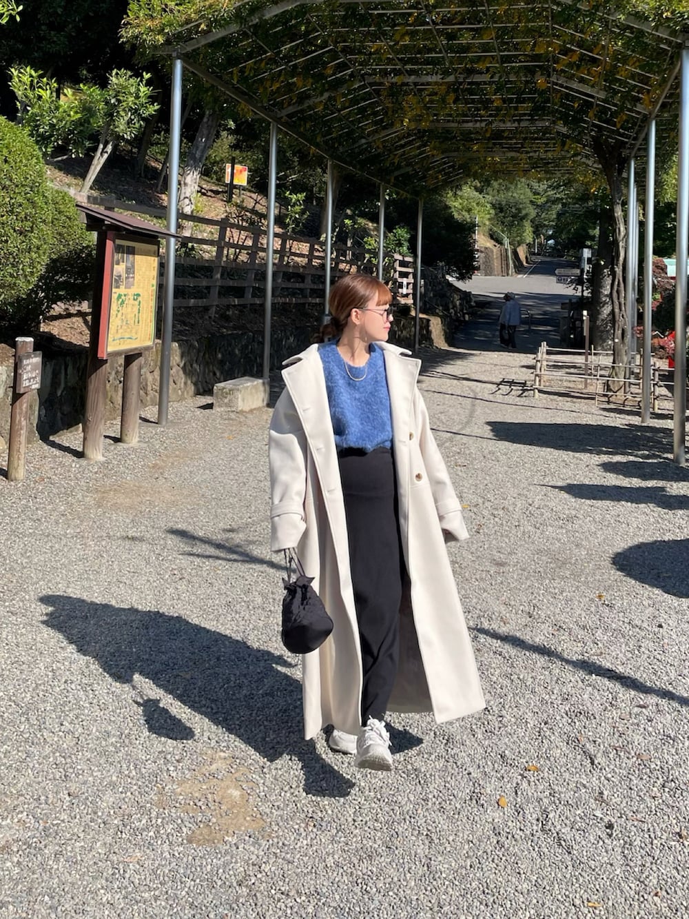 ホワイト系のトレンチコート、ブルー系のニット/セーター、ホワイト系のスニーカーを着用したレディースの秋コーディネートの3枚目の写真