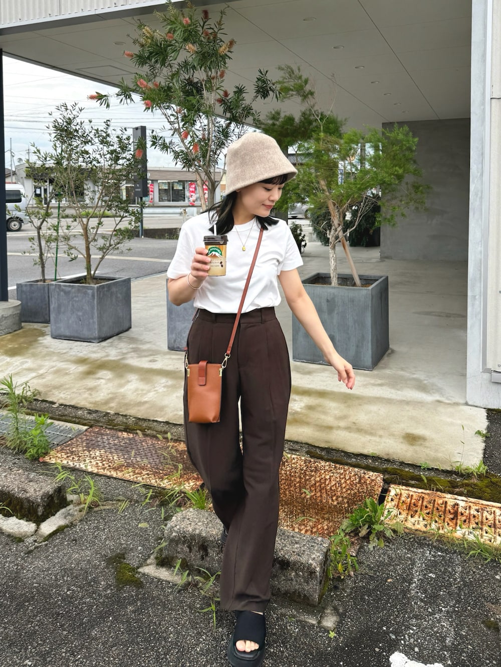 ホワイト系のトップス、ブラウン系のパンツ、ブラック系のサンダルを着用したレディースの夏コーディネートの2枚目の写真