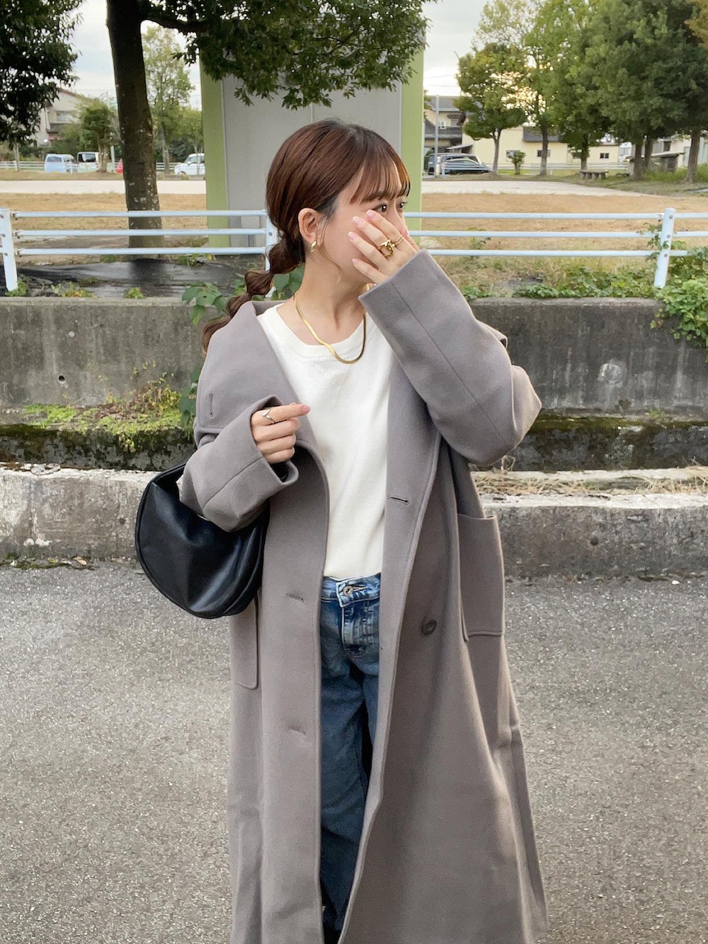 グレー系のトレンチコート、ホワイト系のニット/セーター、ブラック系のハンドバッグを着用したレディースの秋コーディネートの2枚目の写真