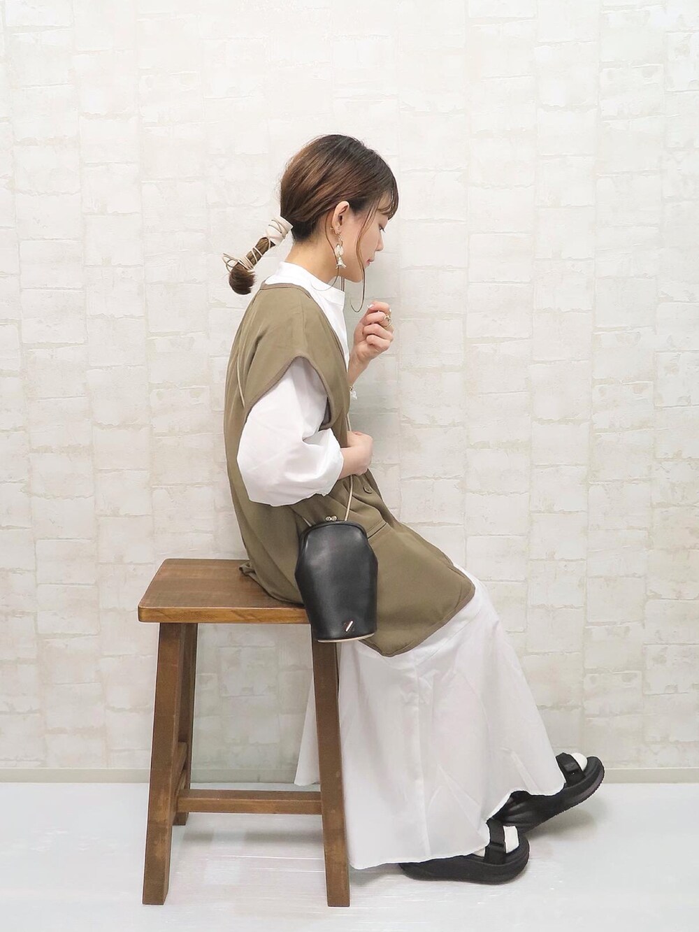 ホワイト系のワンピース、ブラウン系のベスト、ブラック系のショルダーバッグを着用したレディースの春コーディネートの2枚目の写真