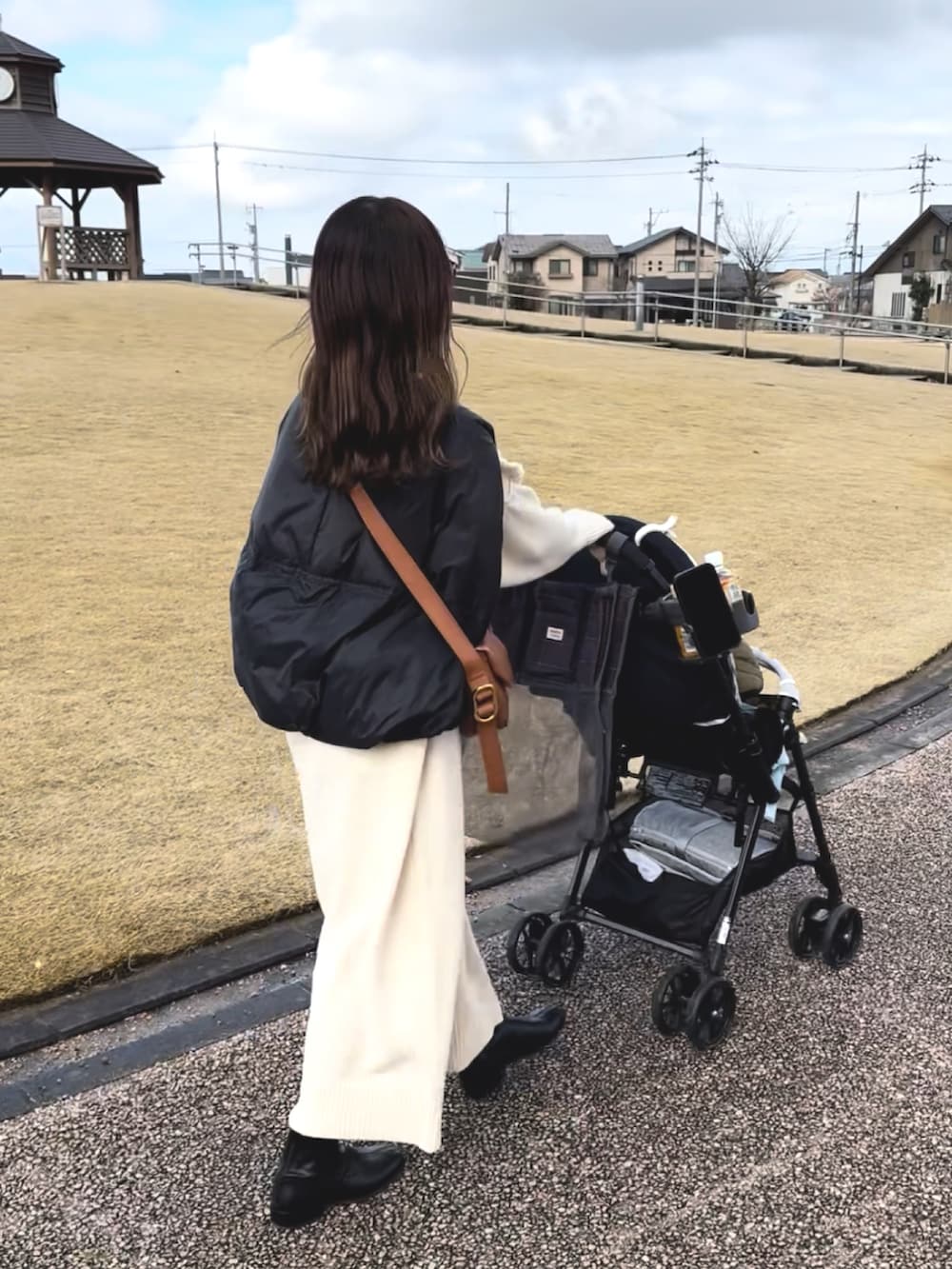 ブラック系のダウンベスト、ホワイト系のワンピース、ブラウン系のハンドバッグを着用したレディースの冬コーディネートの2枚目の写真