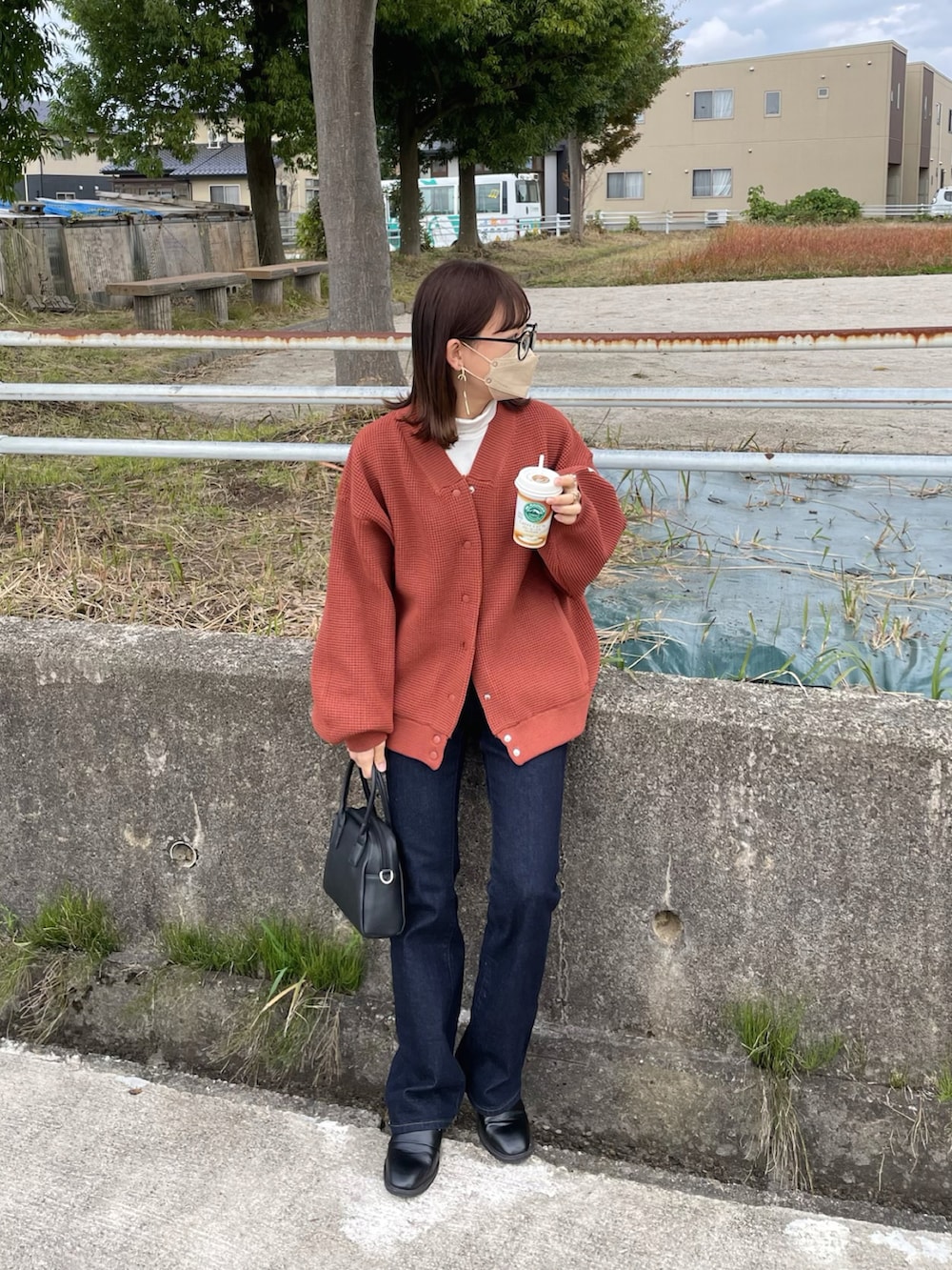 レッド系のカーディガン/ボレロ、ブルー系のデニムパンツ、ブラック系のボストンバッグを着用したレディースの秋コーディネートの2枚目の写真