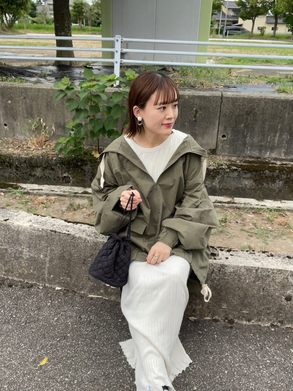 グリーン系のマウンテンパーカー、ホワイト系のワンピース、ブラック系のショルダーバッグを着用したレディースの夏コーディネートの2枚目の写真