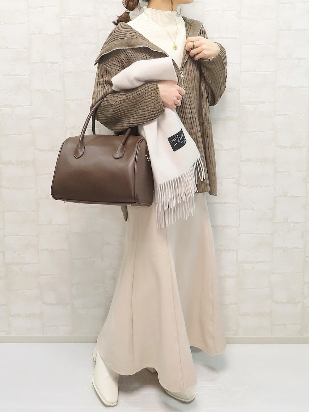 ブラウン系のニット/セーター、ブラウン系のボストンバッグ、ホワイト系のブーツを着用したレディースの冬コーディネートの2枚目の写真