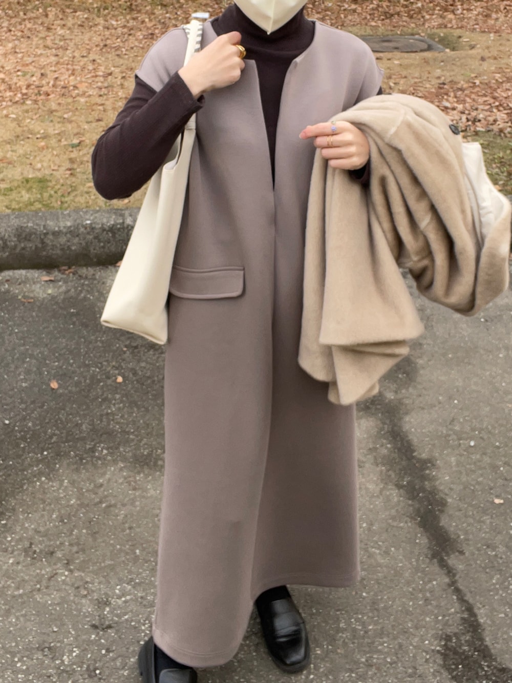 ブラウン系のワンピース、ホワイト系のトートバッグ、ベージュ系のステンカラーコートを着用したレディースの冬コーディネートの3枚目の写真