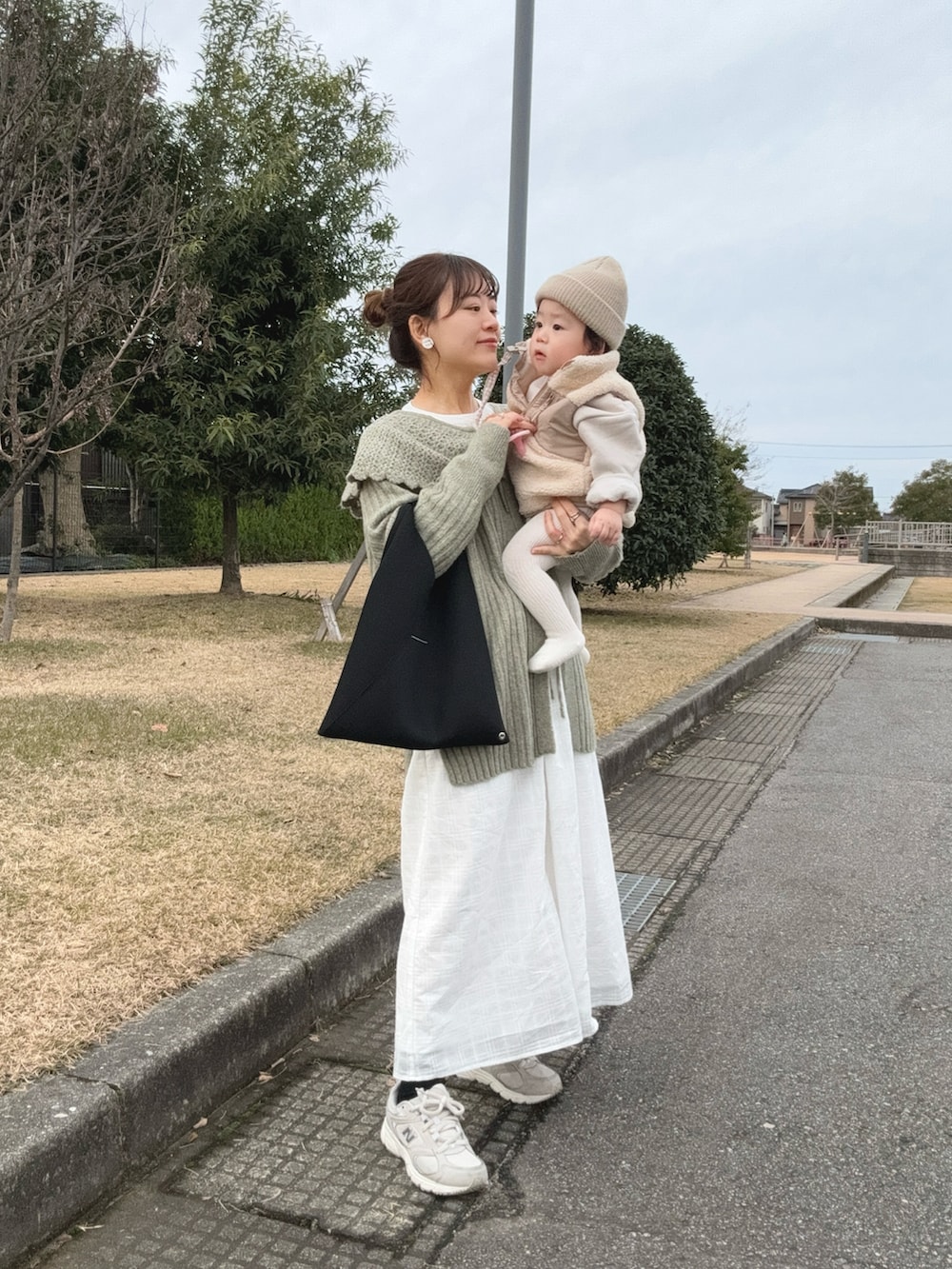 ブラック系のトートバッグ、ホワイト系のスニーカー、グリーン系のカーディガン/ボレロを着用したレディースの冬コーディネートの2枚目の写真