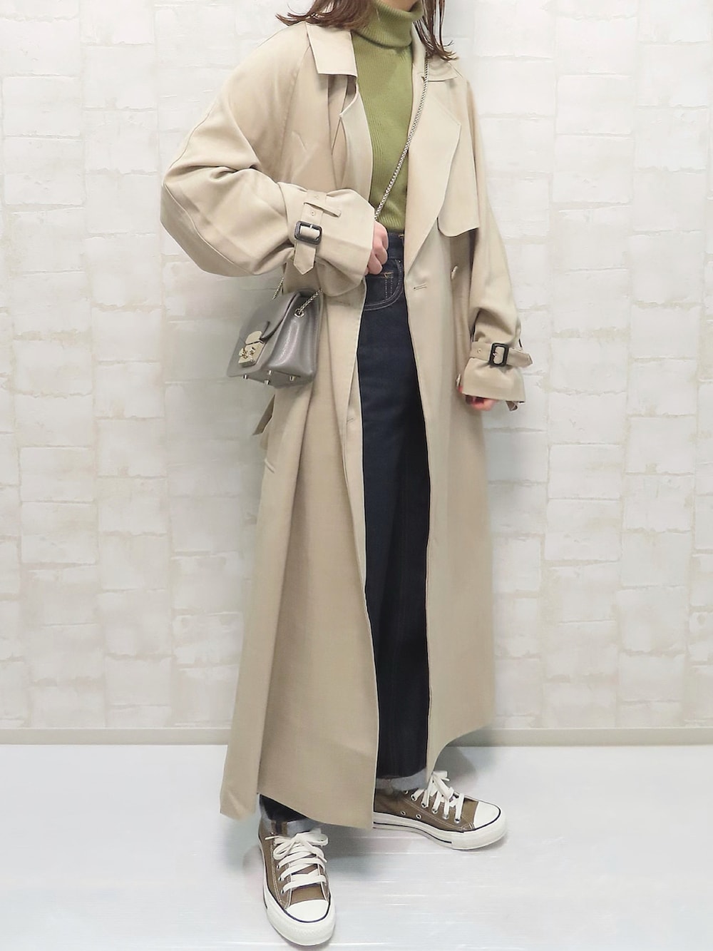 ベージュ系のトレンチコート、グリーン系のニット/セーター、ブルー系のデニムパンツを着用したレディースの冬コーディネートの3枚目の写真